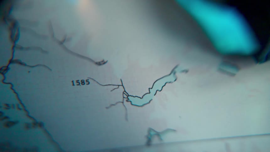 A mysterious close-up shot of a topographical map focusing on a lake or fjord under dim, cool lighting