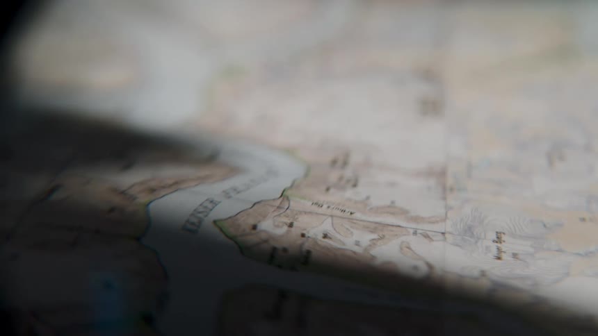 A mysterious close-up shot of an old topographical map, suggesting planning for an expedition or adventure