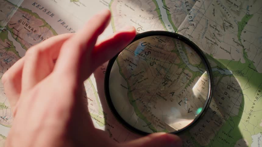 A person uses a magnifying glass to inspect the details on a topographical map while planning an adventure