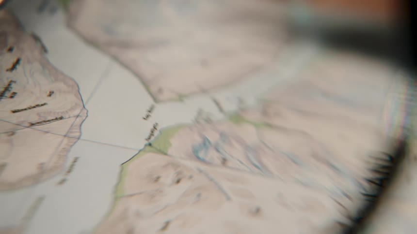 A magnifying glass slowly moves across an old topographical map, suggesting adventure and exploration