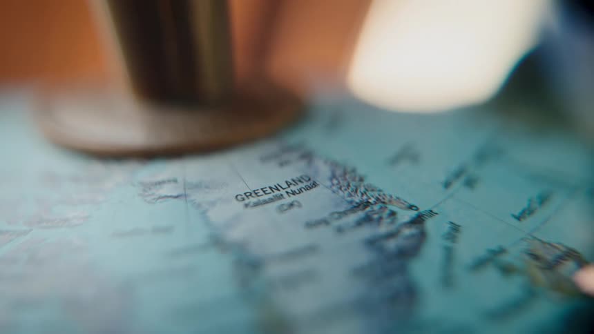 A close-up macro shot focuses on the country of Greenland on a geographical world globe