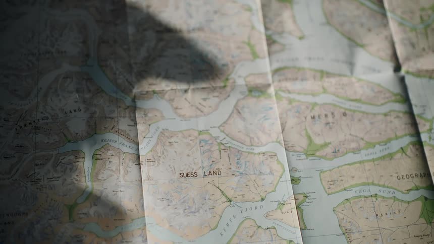 A close-up of a folded topographical map with sunlight casting moving shadows across its surface
