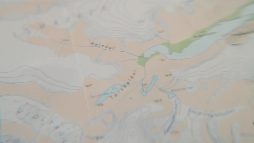 Close-up pan across a detailed topographic map on a wooden table, showing contour lines and geographical features