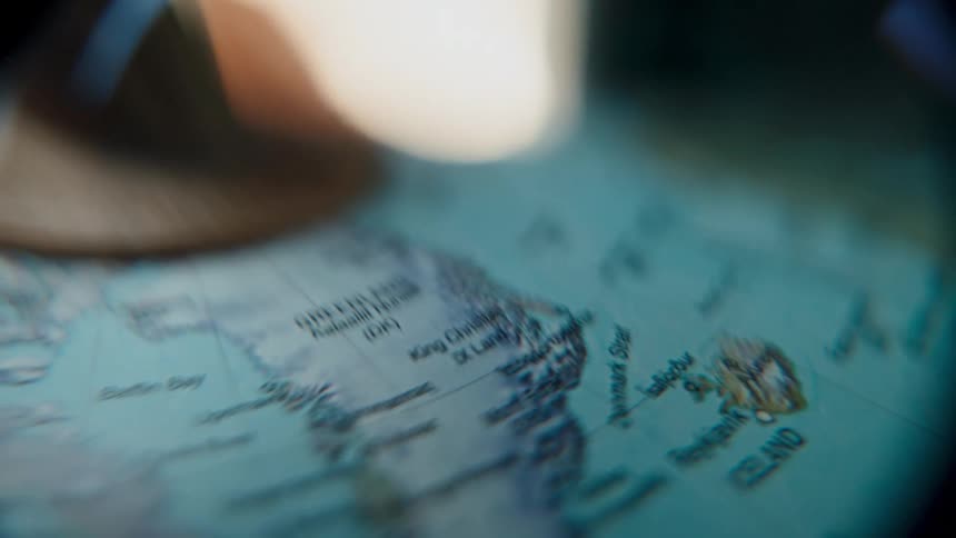 An explorer's magnifying glass slowly pans across a vintage world map, focusing on the icy terrains of Greenland and Iceland