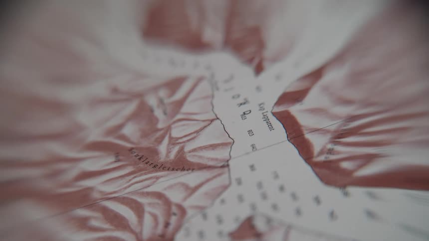 A slow pull-out shot reveals the details of an old, vintage topographical map of a fjord