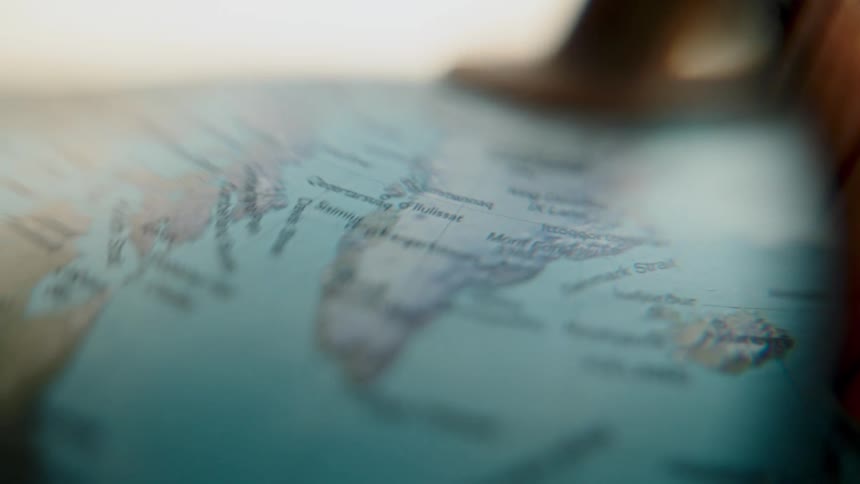 A close-up, artistic view through a magnifying glass scans over Greenland and Iceland on a world map