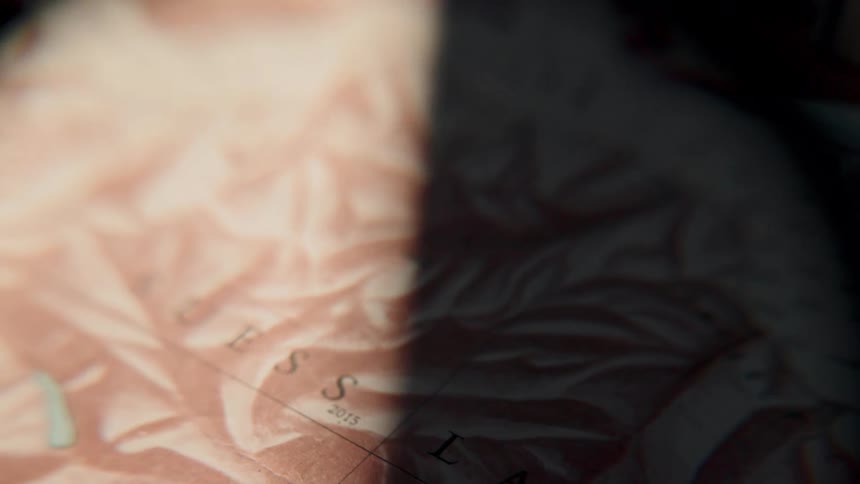 A beam of light from a magnifying glass slowly scans across an old, vintage topographical map, suggesting exploration and adventure