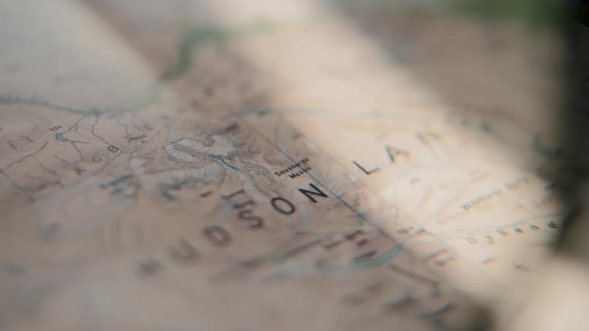 A close-up pan across a topographical map of Hudson Land, illuminated by soft, moving sunlight