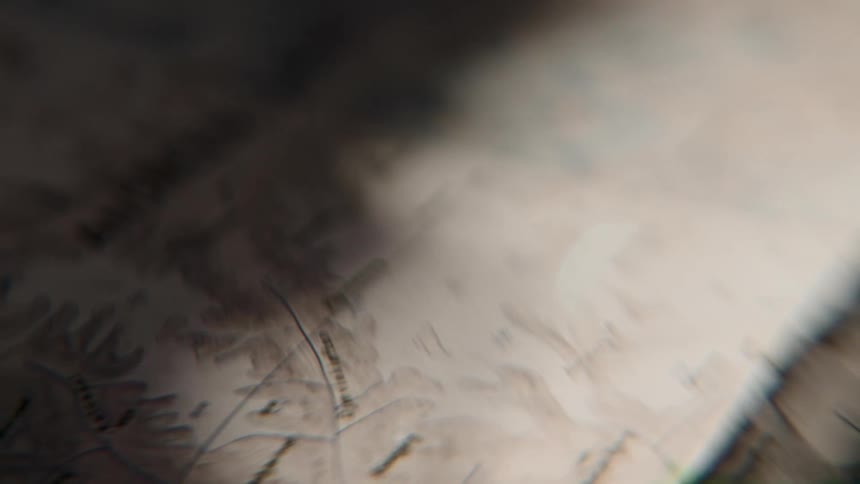 Light scans across a vintage topographical map in a mysterious, close-up shot
