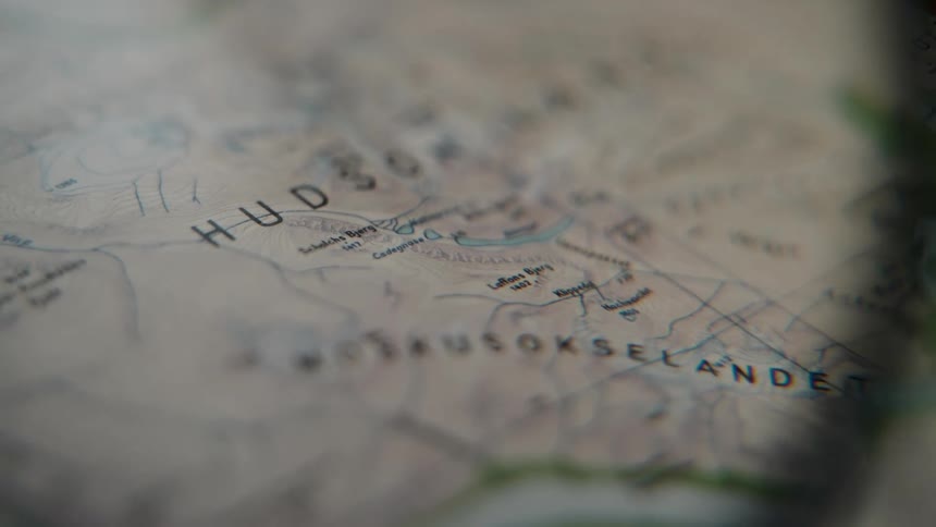 A close-up, shallow focus shot slowly pans across a detailed topographical map, suggesting planning for an expedition or adventure