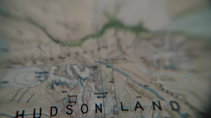 A shallow focus camera slowly pans across a detailed topographical map of Hudson Land, Greenland
