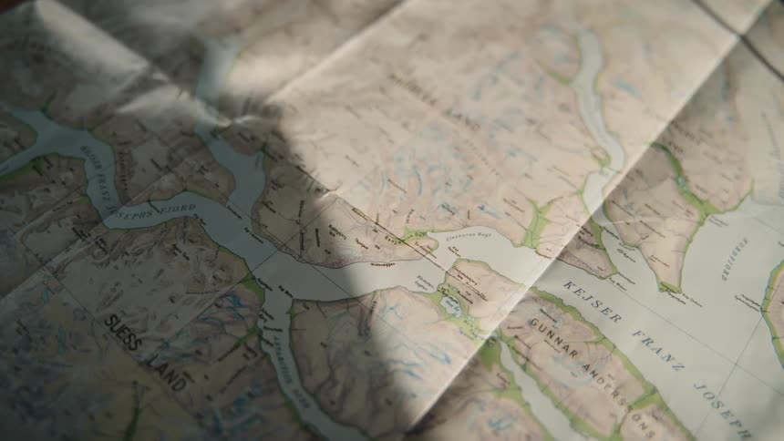 Sunlight and shadows pass over a detailed topographical map of a fjord, suggesting planning for an adventure