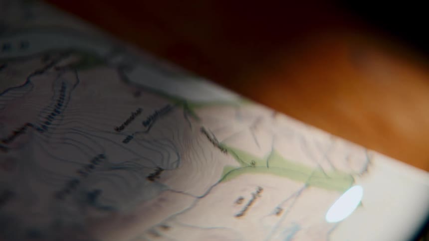 A flashlight beam traces a path across a topographic map, planning an expedition in the dim light