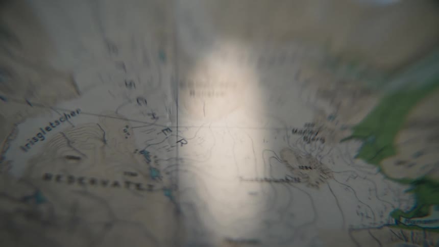 A beam of light slowly moves across a detailed topographical map in the dark