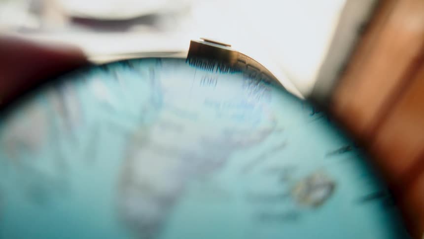 A magnifying glass slowly scans across Greenland and Iceland on a world globe, exploring travel destinations