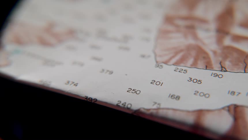 A detailed macro shot slowly pans across an old nautical chart, revealing coastlines and depth soundings