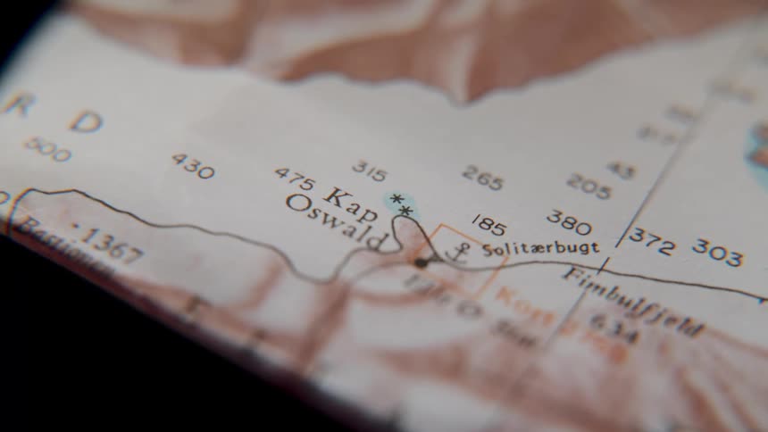 An extreme close-up dolly shot reveals the details of an old, weathered map of a coastline