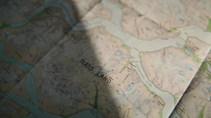 A topographical map of Suess Land, Greenland, is shown with dramatic light and shadows passing over its surface