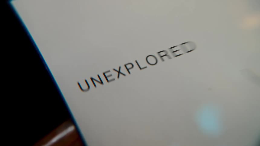 A macro close-up of the word 'unexplored' on a white document being examined through a magnifying glass