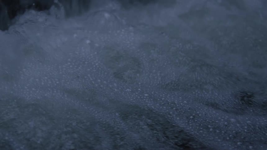 A close-up, slow-motion view of water from a dark cascade creating a turbulent, bubbling flow