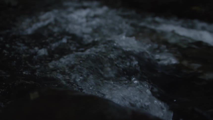 A close-up slow motion shot of a dark river with turbulent water flowing rapidly at night