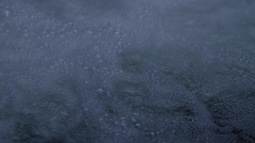 Slow motion close-up of a small waterfall creating frothy white bubbles against a dark background