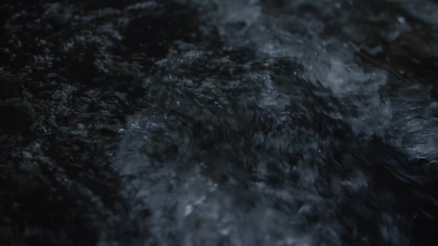 Moody slow-motion close-up of dark water churning and flowing in a stream at night