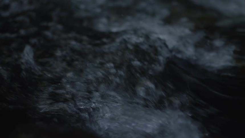 A close-up, slow-motion shot of a dark, turbulent stream flowing rapidly at night