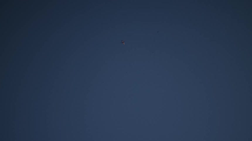 A small kite floats high in the deep blue sky, accompanied by a flock of birds