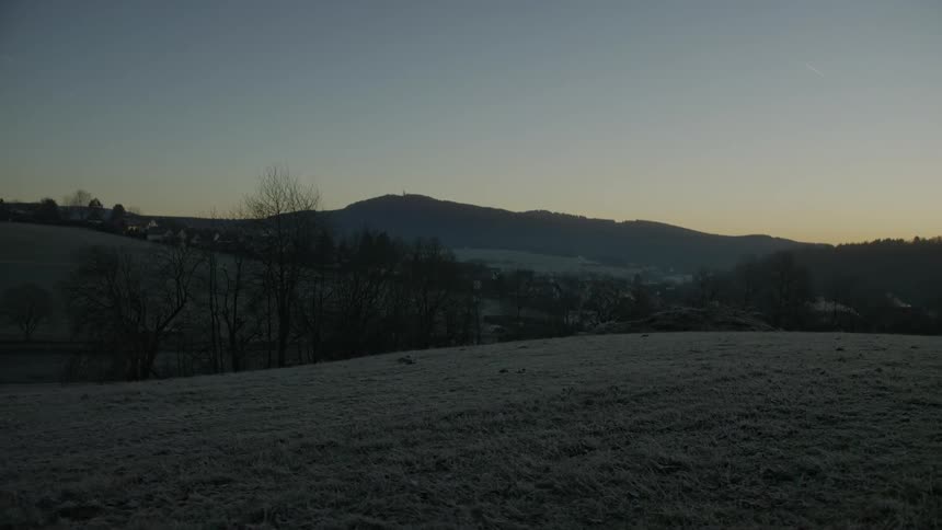 A slow zoom out reveals a frost-covered landscape with a quiet valley and a mountain silhouetted against the dawn sky