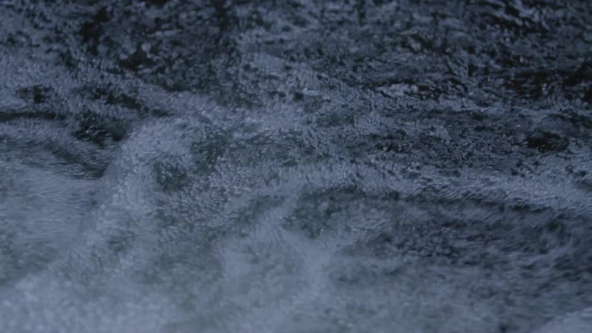 A mesmerizing slow-motion close-up of dark water bubbling and flowing