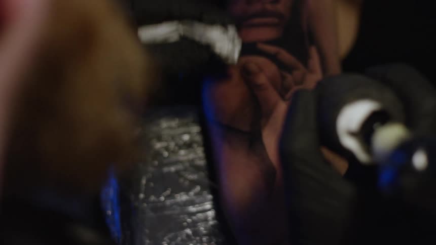 A tattoo artist in black gloves works in slow motion on a realistic portrait tattoo on a client's arm