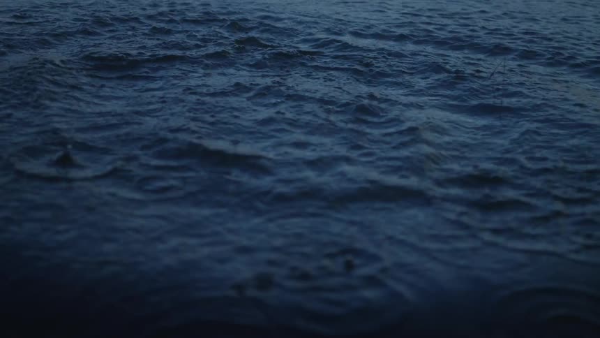 A rock thrown into calm blue water creates a dramatic crown splash in stunning super slow motion