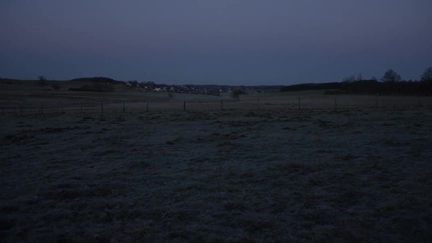 A still shot of a frosty, empty field at dusk with a quiet village in the distance