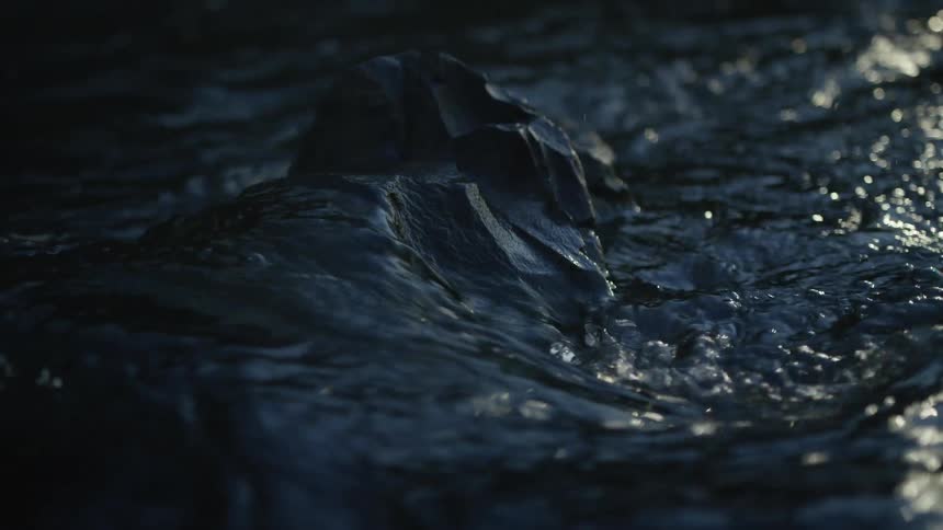 A moody close-up of dark river water flowing gently around a single rock