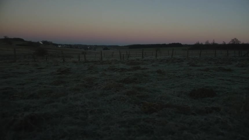 A slow tracking shot over a frosty, rural landscape at dawn with a colorful gradient sky
