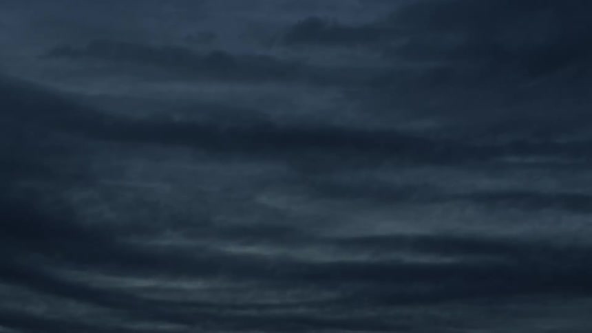 Dark and moody time-lapse of rippled storm clouds rolling across the sky at dusk