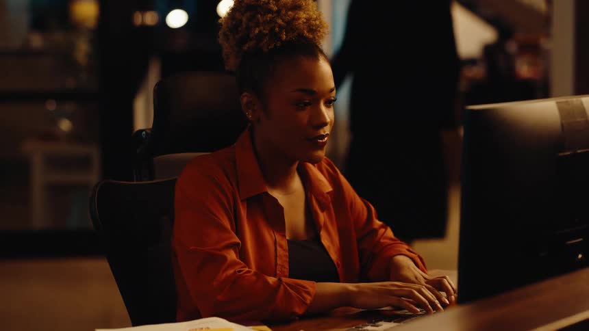 A dedicated businesswoman consults with a colleague while working late at her computer in a modern office