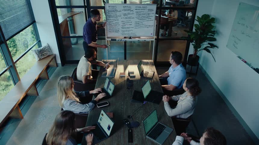 Cinemagraph of a team of professionals in a modern conference room listening to a colleague's presentation at a whiteboard