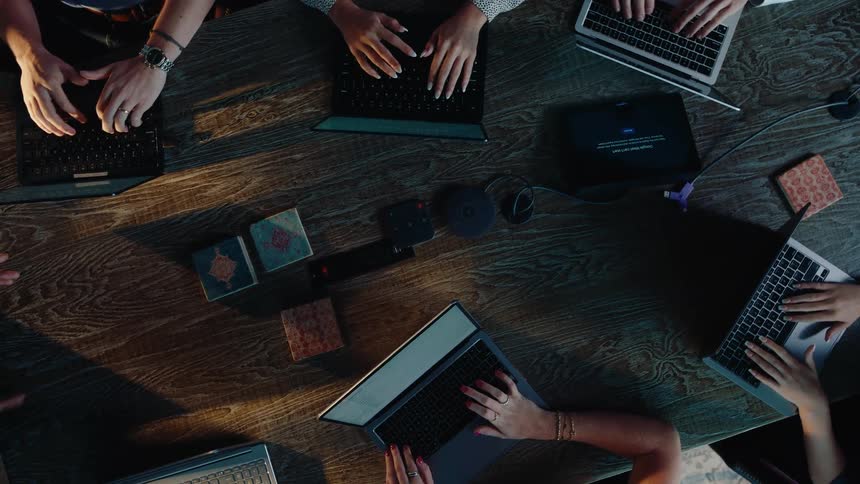 Top-down view of a business team working collaboratively on their laptops around a large wooden conference table