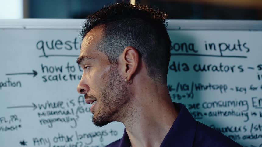 A focused man with a stylish haircut gives a presentation in front of a whiteboard with brainstorming notes