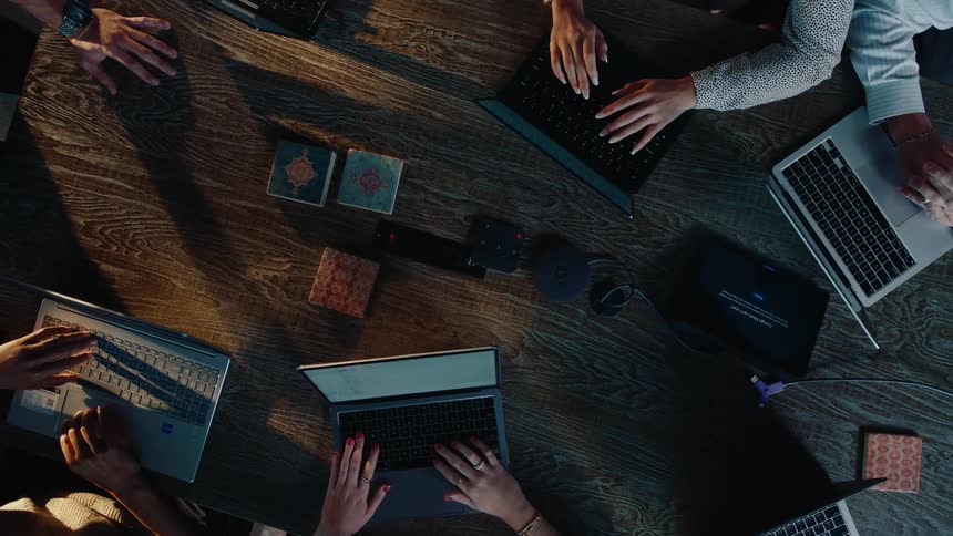 A top-down view of a business team working collaboratively on their laptops around a conference table in a modern office