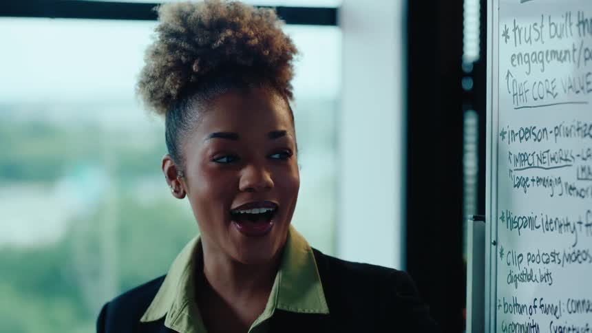 Close up of a professional young woman with curly hair presenting and laughing during a corporate meeting