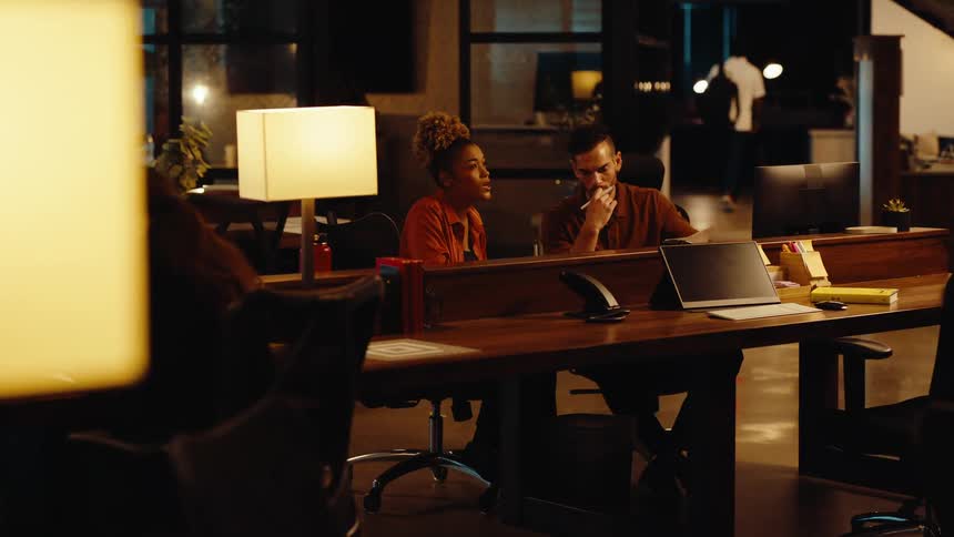 A man and a woman collaborate on a project, reviewing documents together while working late in a modern office