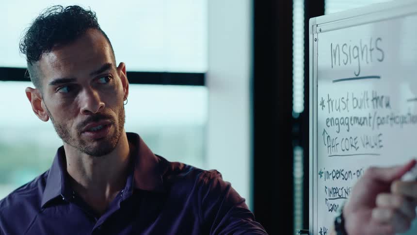 A passionate businessman with a stylish haircut gives a presentation, pointing to insights written on a whiteboard in an office