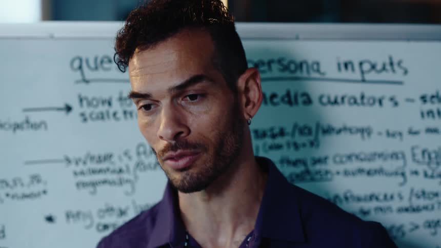 A close-up of a thoughtful man with a modern haircut speaking during a business presentation in front of a whiteboard