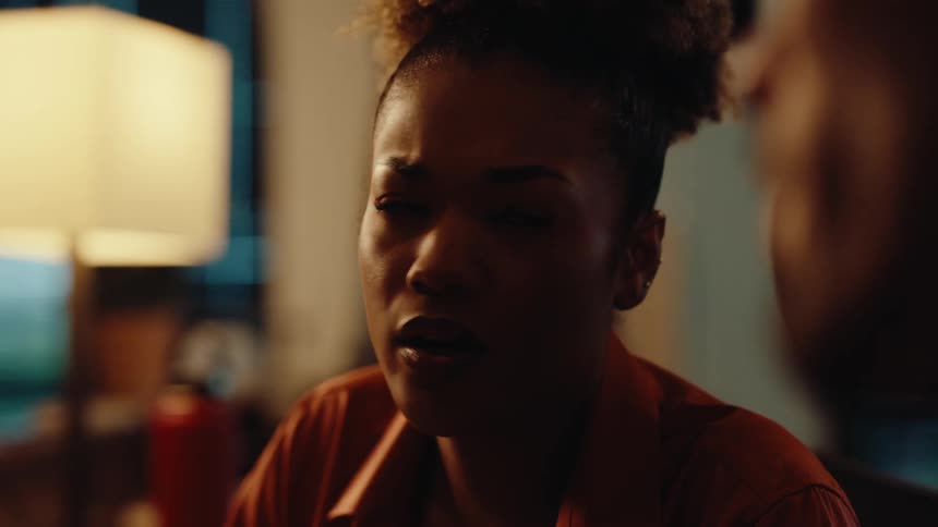 Over-the-shoulder close-up of a young woman having an emotional conversation in a dimly lit room
