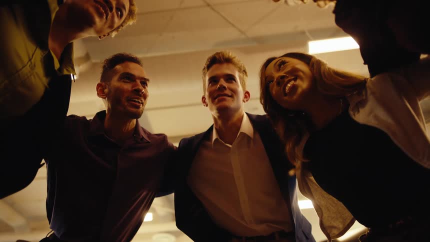 Low angle slow-motion shot of a diverse team of colleagues huddling together in a circle, smiling and celebrating their success