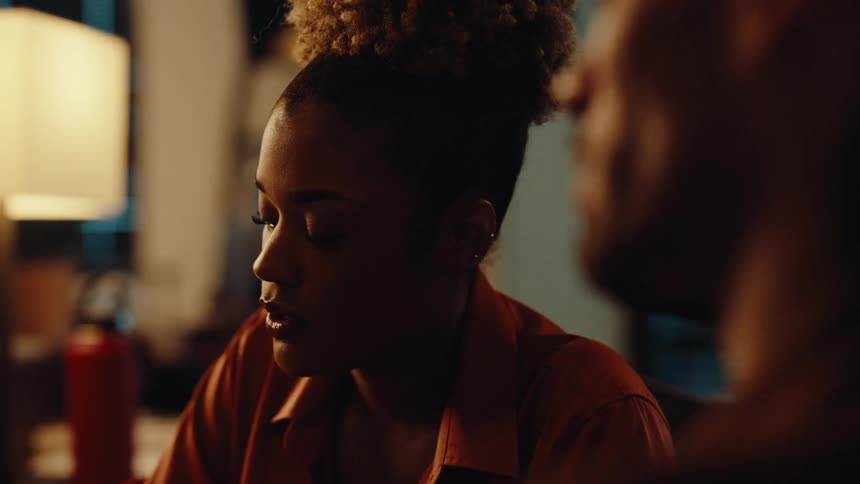 A young woman with a concerned expression listens and speaks during a serious and emotional conversation in a dimly lit room