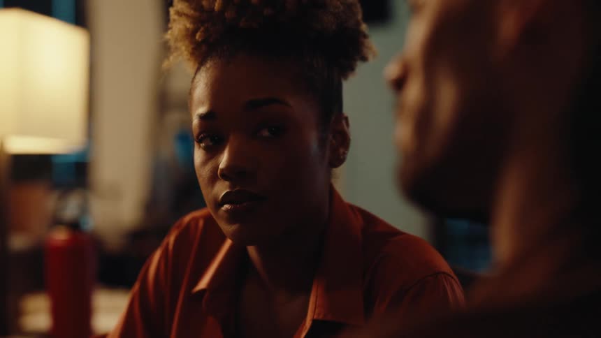 A young woman has an intimate and serious conversation with a man in a warmly lit room at night